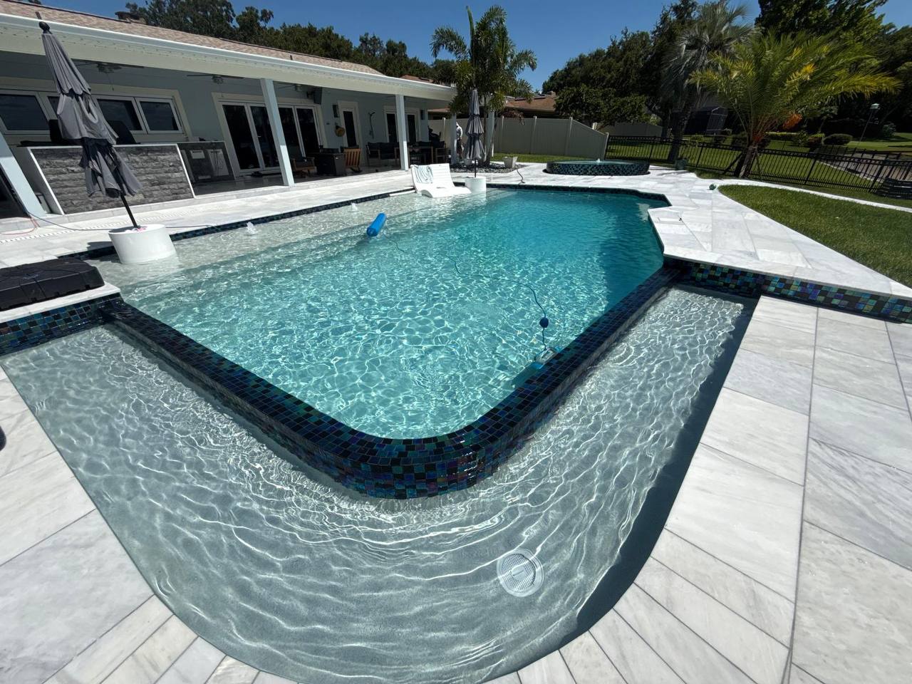 Modern renovated pool with elegant blue tile work and professional landscaping